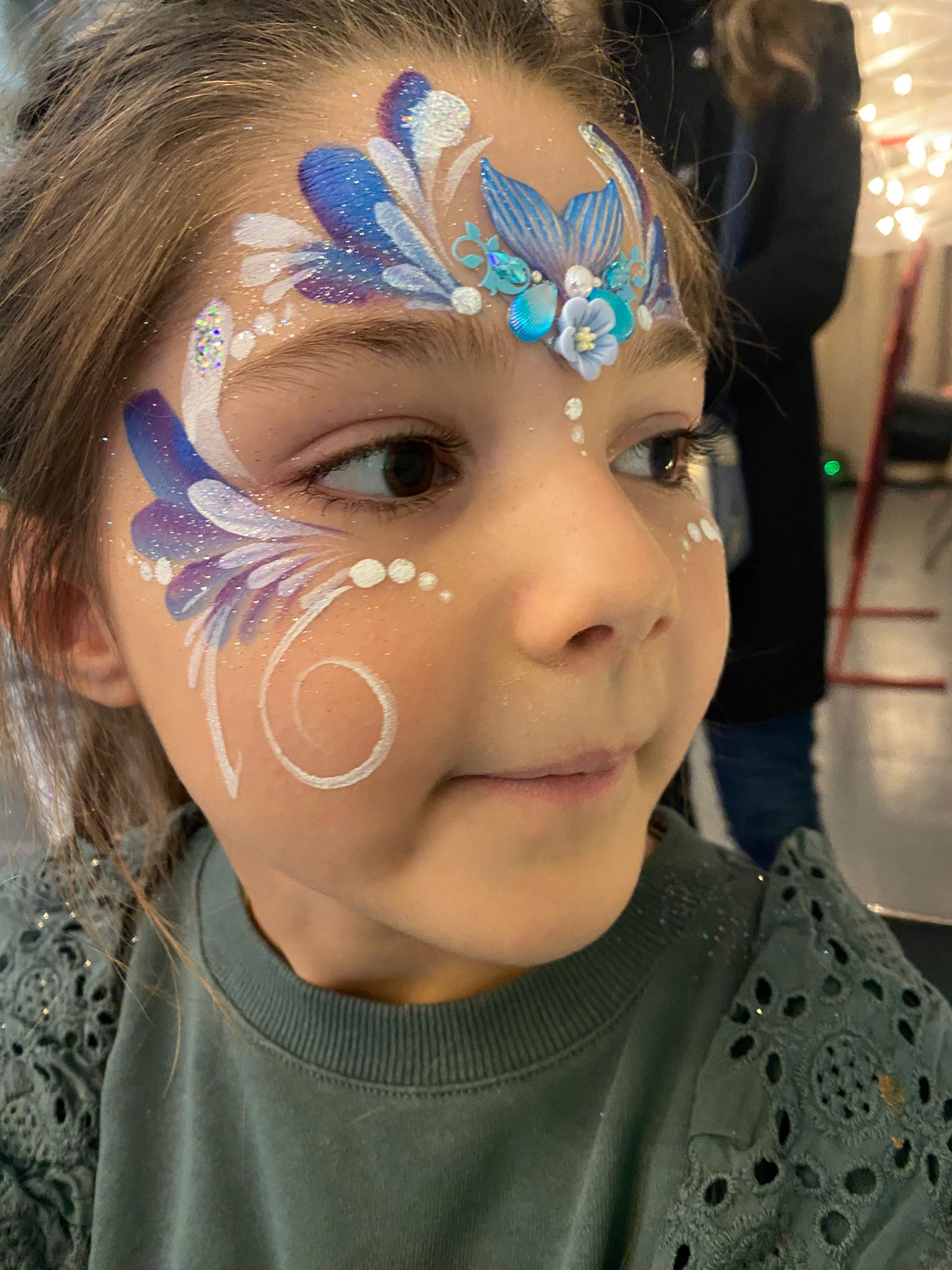 Enfant avec maquillage papillon violet et bleu agrémenté de strass turquoise et fleurs