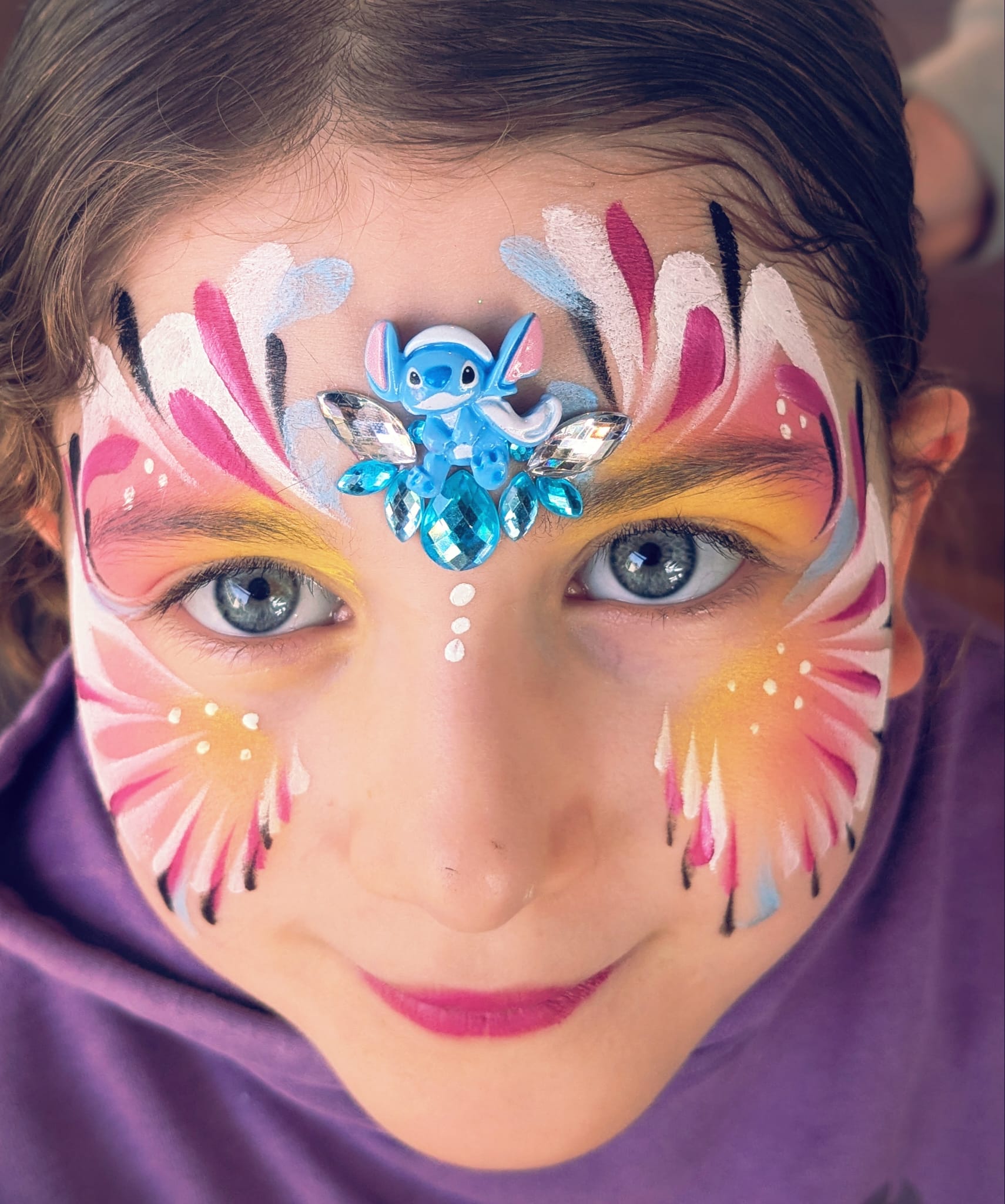 Maquillage papillon rose et jaune avec figurine Stitch et pierres strass sur le visage d une enfant